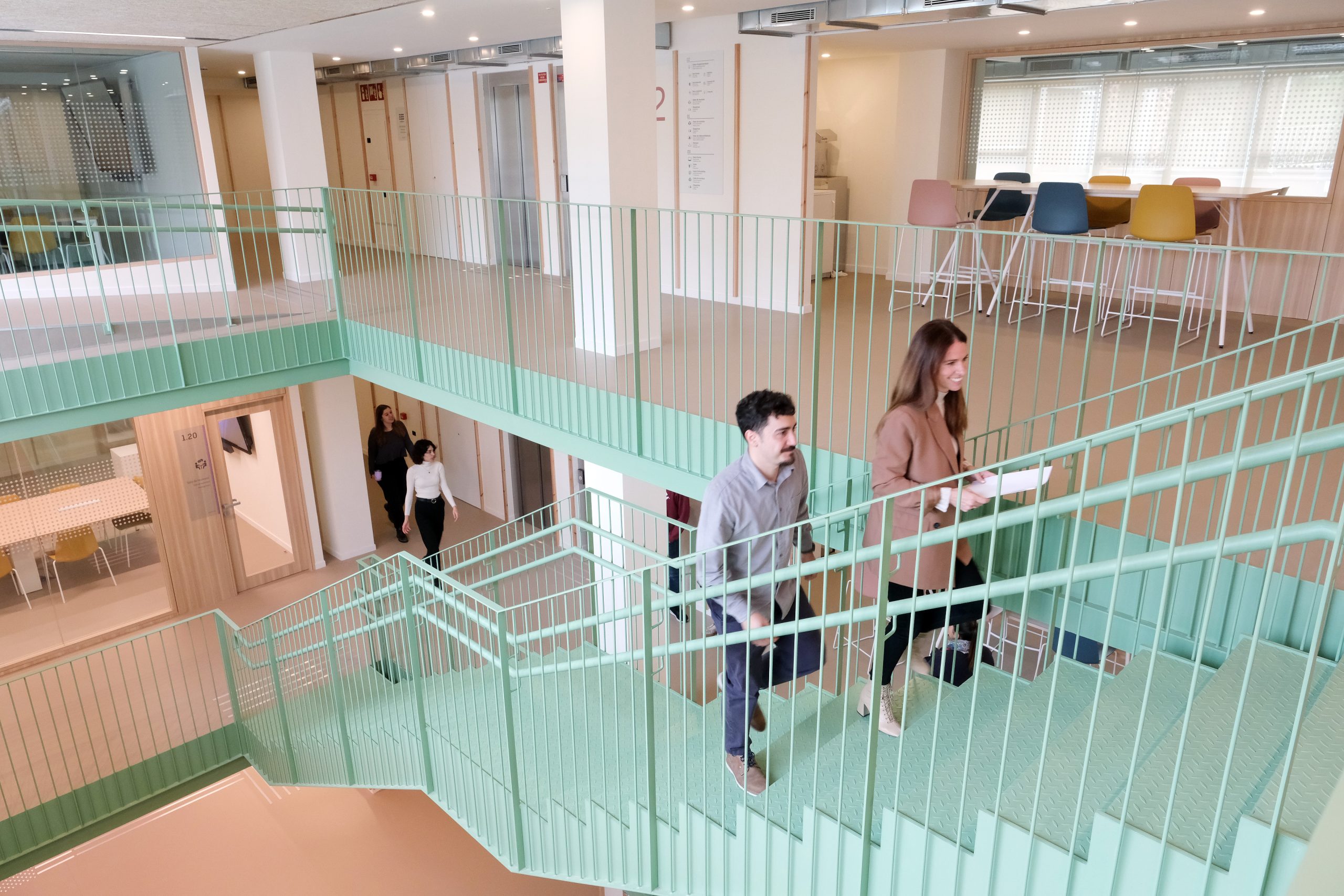 Persones pujant escales verdes a l’interior lluminós de l’edifici Somrise.